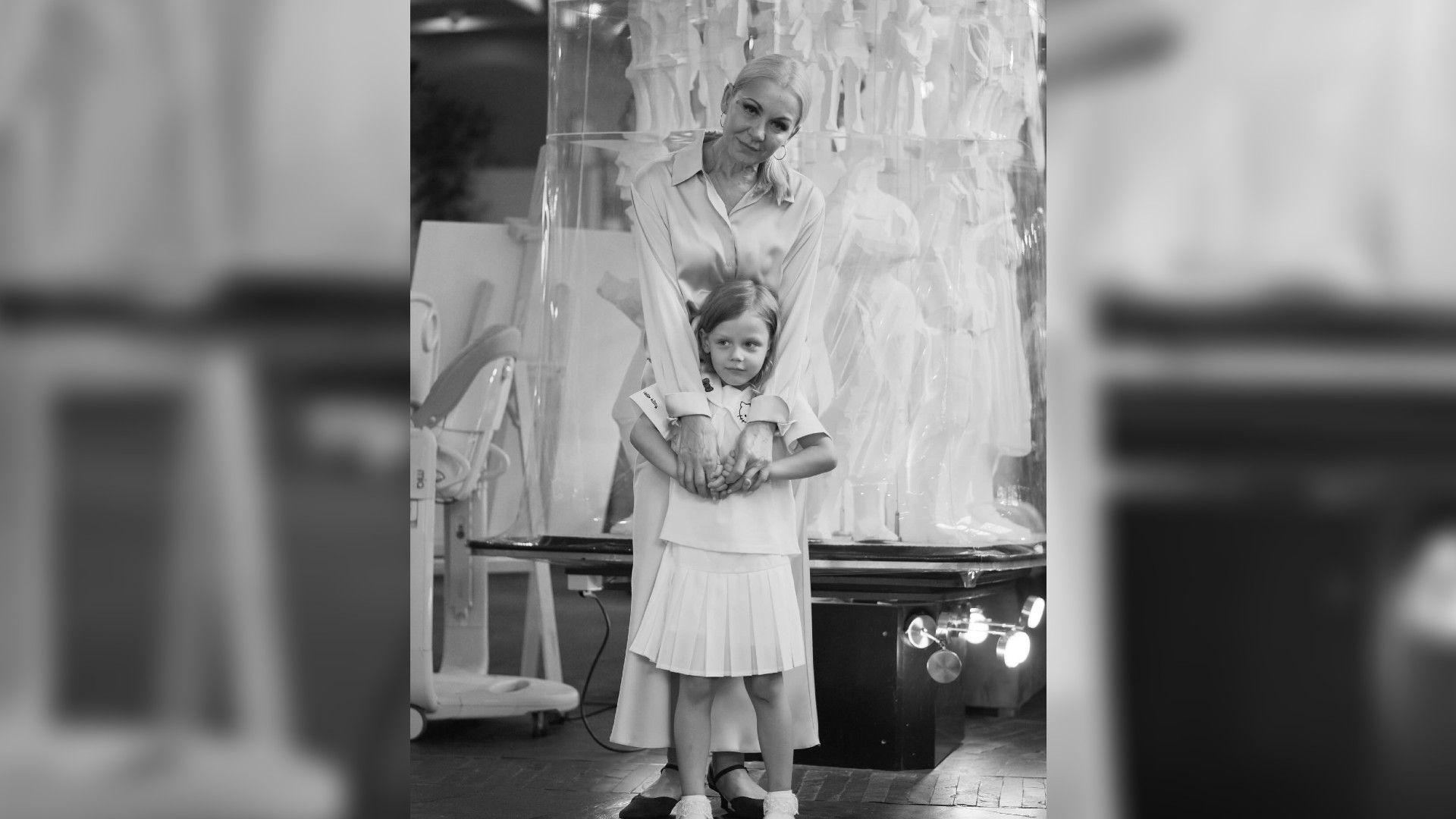 Марина Зудина в светлом платье нежно обнимает маленькую девочку, стоящую перед ней